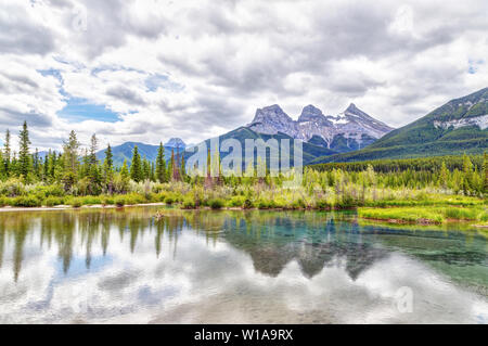 Weitwinkelaufnahme der Canmore berühmten Three Sisters Berggipfel und deren Reflexionen auf dem Bow River im südlichen Bereich des kanadischen Banff Ro Stockfoto