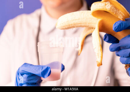 Weibliche Ärzte die Hände in der medizinischen blaue Handschuhe Holding ein Kunststoffbehälter mit Sperma und eine Banane. Medizinisches Konzept von Spermien testen, künstliche insemina Stockfoto