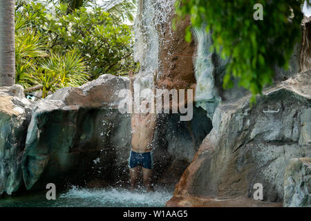 Ein junger Kerl steht unter künstlichen Wasserfällen in den Pool zur Verfügung. Stockfoto