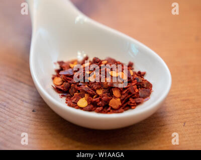 Türkische Paprika Flocken in einem weißen Porzellan Löffel auf einen hölzernen Tisch Stockfoto