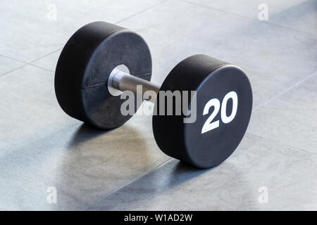 Fitness oder Bodybuilding Konzept Hintergrund. Schwarzes Eisen Hantel auf dem Boden in der Turnhalle. Stockfoto