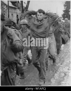 Ein Schlaksiger GI, mit gefalteten Händen hinter seinem Kopf, führt eine Datei der amerikanischen Gefangenen entlang einer Straße marschierend irgendwo an der Westfront. Die deutschen Diese amerikanischen Soldaten während der überraschung Feind Laufwerk in Alliierten Positionen erfasst.; Allgemeine Hinweise: Verwenden Sie Krieg und Konflikt Nummer 1071 bei der Bestellung eine Reproduktion oder Anforderung von Informationen zu diesem Bild. Stockfoto