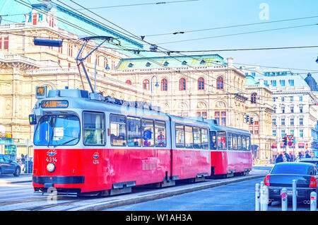 Wien, Österreich - 18. FEBRUAR 2019: Die rote Straßenbahn fährt auf der Straße in der Innenstadt mit der Oper auf dem Hintergrund, am 18. Februar in V Stockfoto