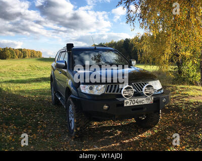 Mitsubishi Pajero Sport und Bäume im Herbst an einem sonnigen Tag. Moskau, Russland. Oktober 12, 2018 Митсубиси Пажеро спорт припаркован осенью на природе Stockfoto