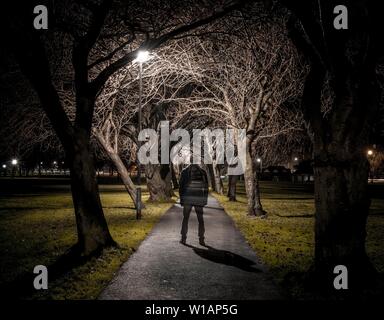 Geisterhafte Silhouette einer dunklen Person auf einen Pfad durch eine Allee an der Nacht, trübe Stimmung, Krönung Spaziergang im Meadows Park, Edinburgh, Schottland Stockfoto