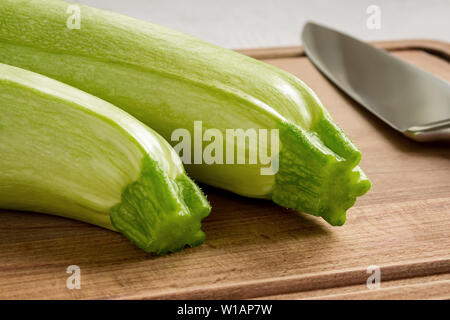 Zwei frische grüne Zucchini und professioneller Koch Messer auf einem braunen Holz Schneidebrett. Zu Hause kochen. Frisches Gemüse und Gesunde vegetarische Kost. Cl Stockfoto