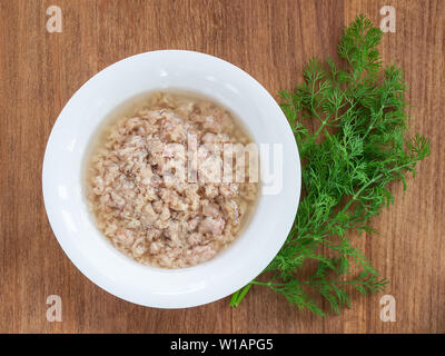 Weiße Porzellanschale mit geschredderten Thunfisch in Öl zum Kochen Salat und grünen Dill auf einer hölzernen Hintergrund. Meeresfrüchte, gesundes Essen und Kochen zu Hause conce Stockfoto