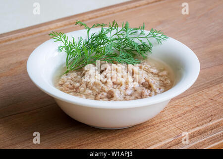 Weiße Porzellanschale mit geschredderten Thunfisch in Öl für einen Salat und grünen Dill auf einer hölzernen Hintergrund. Meeresfrüchte, gesundes Essen und Kochen zu Hause Konzept. Stockfoto