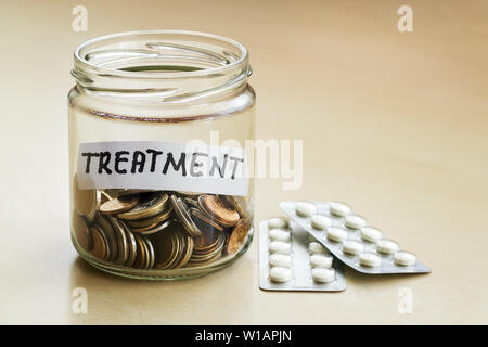 Eine Menge Münzen und Behandlung Wort in einem Glas in der Nähe von zwei Blasen mit Pillen auf einen Tisch. Geld sparen für die Behandlung Konzept. Planung für die Zukunft. Stockfoto