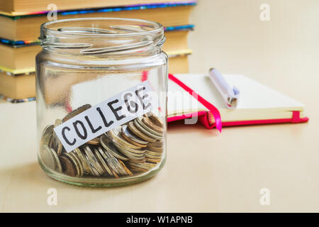 Eine Menge Münzen und College Wort in einem Glas in der Nähe eines weißen Kugelschreiber und einige Bücher auf einem Tisch. Geld sparen für Hochschule und Bildung Konzept. Pl Stockfoto