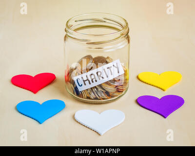 Eine Menge Münzen und liebe Wort in einem Glas in der Nähe von fünf bunte Herzen. Speichern und Sammeln Geld für wohltätige Zwecke. Stockfoto