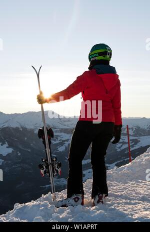 Weibliche Skifahrer mit Ski Helm mit Ski an der Skipiste, in die Ferne suchen, Bergen und auf der Rückseite, der SkiWelt Wilder Kaiser, Brixen im Stockfoto