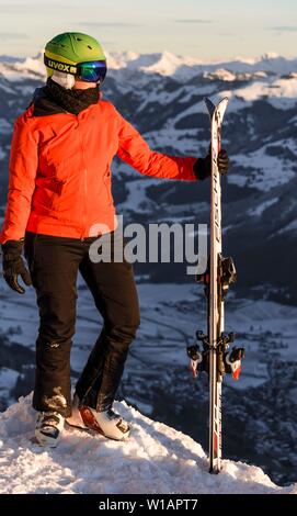 Weibliche Skifahrer mit Ski Helm mit Ski auf der Piste über dem Tal, auf die Seite Suchen, Berge hinter, SkiWelt Wilder Kaiser Stockfoto