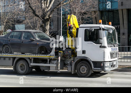 Varna, Bulgarien, 28. Februar 2019. Ein Abschleppwagen mit Haken und Kette transportiert einen Wagen ohne Vorderrad entlang der Straße der Stadt während des Tages. Die c Stockfoto