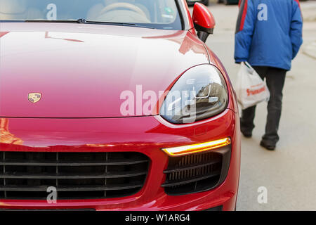 Varna, Bulgarien, 28. Februar 2019. Ein schlecht gekleideter älterer Mann auf der Straße hinter einem roten Porsche Auto. Konzept von Luxus und Armut. Kontrast Stockfoto