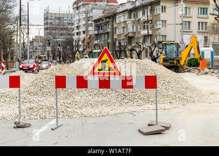 Das Zeichen der Straße arbeiten auf Rot Weiß Barriere vor einem Stapel von Kies auf einer Straße der Stadt. Bau und Reparatur von asphaltierten Straßen in einer Stadt. Stadt im Stockfoto