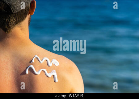 Junger Mann mit Wave-gebildet Sonnencreme auf seiner Schulter stehen am Strand, über dem Meer Stockfoto