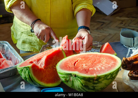 Nahaufnahme einer Frau schneiden bis eine Wassermelone mit einem Messer auf einer Küchenarbeitsplatte. Stockfoto