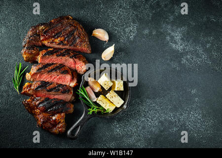 Ribeye Steak in Scheiben, gegrillt mit Pfeffer, Knoblauch, Salz und Thymian auf einem dunklen Stein Hintergrund. Ansicht von oben. Flach. Stockfoto