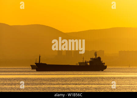 Golden Sunset, Silhouette der Stadt und Frachtschiff. Schöne architecort durch das Meer auf dem Hintergrund der Sonnenuntergang. Stockfoto