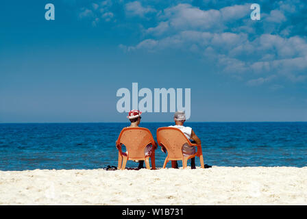 Ältere Paare sitzen auf Plastikstühlen am Strand gegen das Meer. Ansicht von hinten Stockfoto