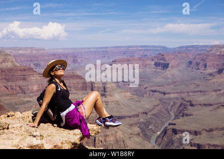 Touristische Frau sitzen und genießen die Sonne in der Nähe einer Klippe in South Rim, Grand Canyon National Park, Arizona, USA Stockfoto