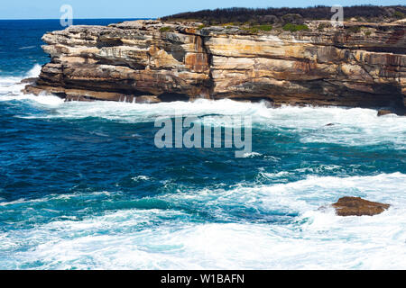 Oceanside rocky Sandsteinfelsen mit blauen Meer Wasser Wellen erzeugen Whitewash gegen Küste und klaren Himmel im Hintergrund Stockfoto