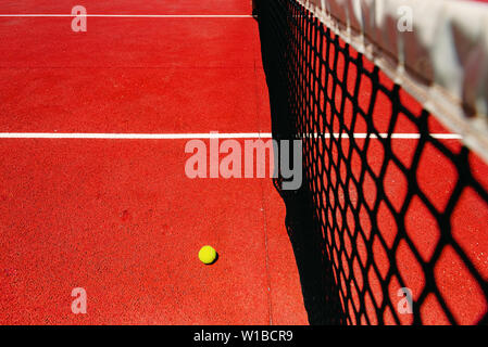 Ein Tennisball auf der texturierten Stock eines roten Hof in der Nähe des Net nach Verlust Match Point. Stockfoto