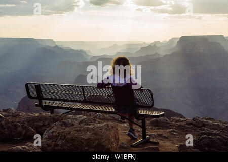 Zurück Kaukasischen, lockigen Haaren touristische Frau beobachten Sonnenuntergang von einer Bank in Desert View, Grand Canyon National Park, Arizona, USA Stockfoto