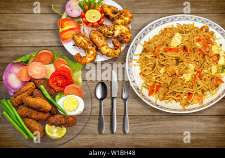 Indisches essen Mahlzeit von spicy Chicken chowmein Nudeln mit knusprige Fischstäbchen und frittierte Garnelen mit Salat serviert. Stockfoto