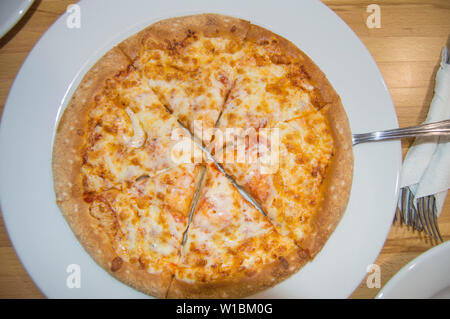 Frisch gebackenen Käse Pizza, appetitlich in Stücke schneiden liegt auf einem weissen Teller, Ansicht von oben in der Tabelle und Besteck. Stockfoto