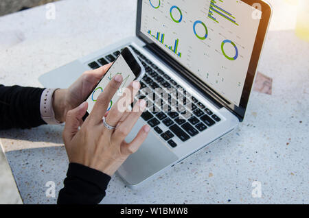 Geschäftsfrau Arbeiten im Freien sitzen, Laptop und Smartphone mit Grafiken, Diagrammen und Tabellen auf dem Bildschirm. Stockfoto