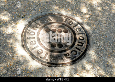 Telefónica Gusseisen Schachtdeckel mit Logo, auf einer schattigen Bürgersteig in Granada, Spanien. Stockfoto