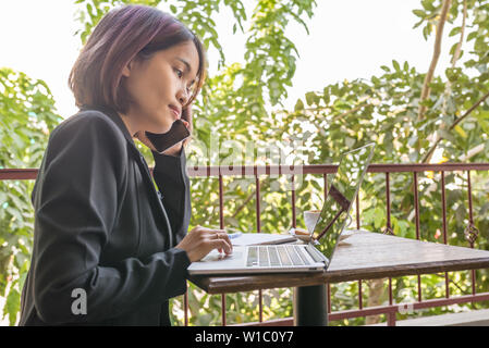 Frau in Schwarz mit Handy und Laptop Anzug Stockfoto