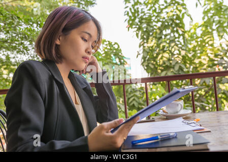 Hart arbeitende Frau im schwarzen Anzug lesen Dokument in Garten Hintergrund Stockfoto