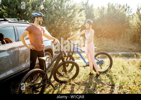 Junges Paar in Sportkleidung mit Mountainbikes in der Nähe des Auto, Vorbereitung für das Fahrrad fahren im Wald Stockfoto