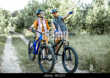 Junges Paar reisen mit Mountainbikes im Wald, man zeigt mit der Hand auf den Weg in die Zukunft Stockfoto