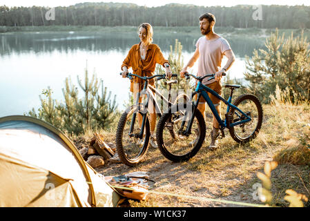 Junges Paar mit Mountainbikes auf dem Campingplatz, im Wald, in der Nähe des Sees auf dem Sunset Stockfoto