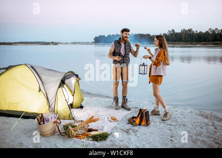 Junges Paar, das Spaß am Campingplatz am Strand, in der Nähe der Feuerstelle am Abend Stockfoto