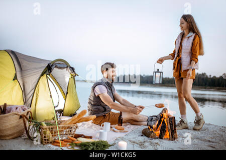 Junges Paar, das Spaß am Campingplatz am Strand in der Nähe der Feuerstelle am Abend Stockfoto