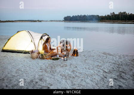 Junges Paar auf dem Campingplatz am Strand sitzen, Mann kindling Fire Stockfoto