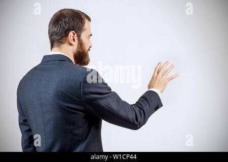 Geschäftsmann in Anzug zeigt ausgestreckte Hand withspread Finger. Über grauen Hintergrund. Ansicht von hinten. Stockfoto