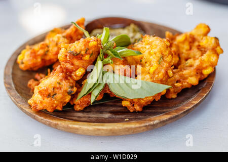 Perkedel Jagung oder bakwan Jagung, Mais Krapfen mit Sambal hijau (grüne Chili-Sauce) auf einem Holzteller serviert. Indonesische Küche. Stockfoto