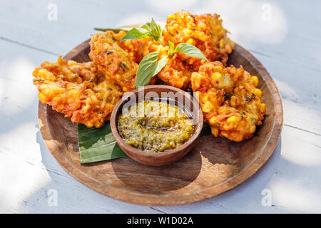 Perkedel Jagung oder bakwan Jagung, Mais Krapfen mit Sambal hijau (grüne Chili-Sauce) auf einem Holzteller serviert. Indonesische Küche. Stockfoto