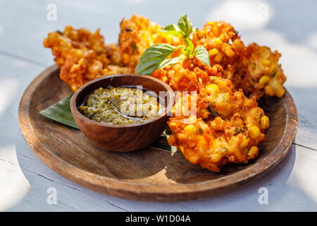 Perkedel Jagung oder bakwan Jagung, Mais Krapfen mit Sambal hijau (grüne Chili-Sauce) auf einem Holzteller serviert. Indonesische Küche. Stockfoto