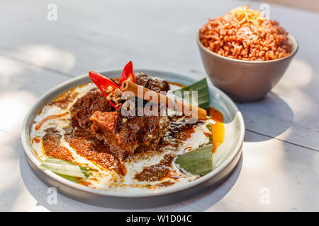 Beef Rendang auf einem Teller mit Banana Leaf, mit rotem Chili und Zimtstange dekoriert. Mit nasi Merah serviert, gedünsteten Roten Reis. Indonesische Küche. Stockfoto
