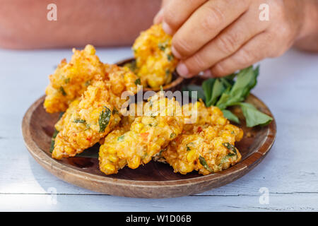 Perkedel Jagung oder bakwan Jagung, Mais Krapfen mit Sambal hijau (grüne Chili-Sauce) auf einem Holzteller serviert. Indonesische Küche. Stockfoto