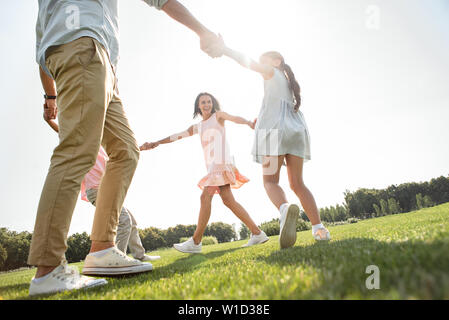 Tanzen zusammen. Glückliche Familie halten sich an den Händen und tanzen im Kreis auf der Wiese beim verbringen die Zeit zusammen im Freien. Liebe und Familie Konzept Stockfoto