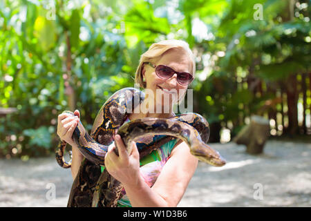 Frau mit python Schlange in Tropical Zoo. Dame beobachten exotische Reptil. Weibliche Touristen mit Schlangen auf Reise Park zu Safari. Menschen beim Lernen zu overco Stockfoto