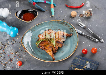 Gegrillte Wachteln mit Sauce mit schwarzem, weißem Pfeffer und Salz Gewürze. Chili und Cherry Tomaten für Ihr Rezept. Messer und Gabel auf Stein bac serviert. Stockfoto